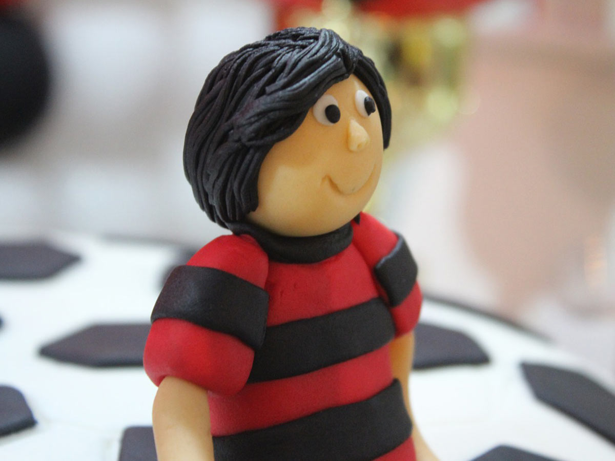 Figure of a boy, made from fondant icing, wearing a striped football shirt.
