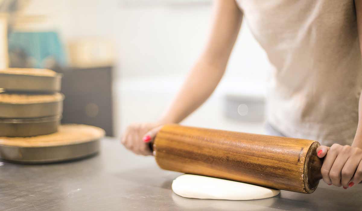 Woman rolling out dough on the worktop using a rolling pin.