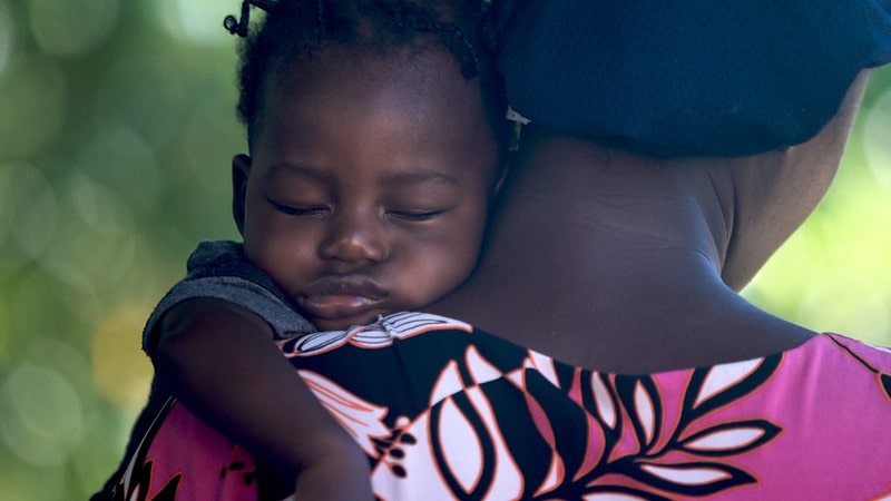 Baby girl sleeping on her mum's shoulder in her arms.