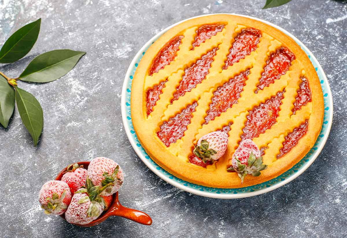 A big, latticed strawberry jam tart and a bowl of strawberries on the side.