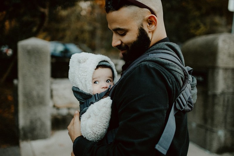 Dad looking down at his baby lovingly, who is in a baby sling.