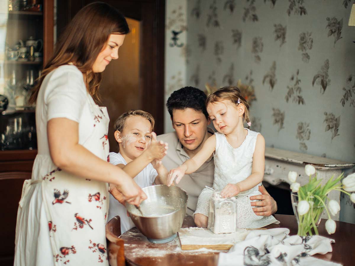 Family of four in the kitchen baking a panda cake together.