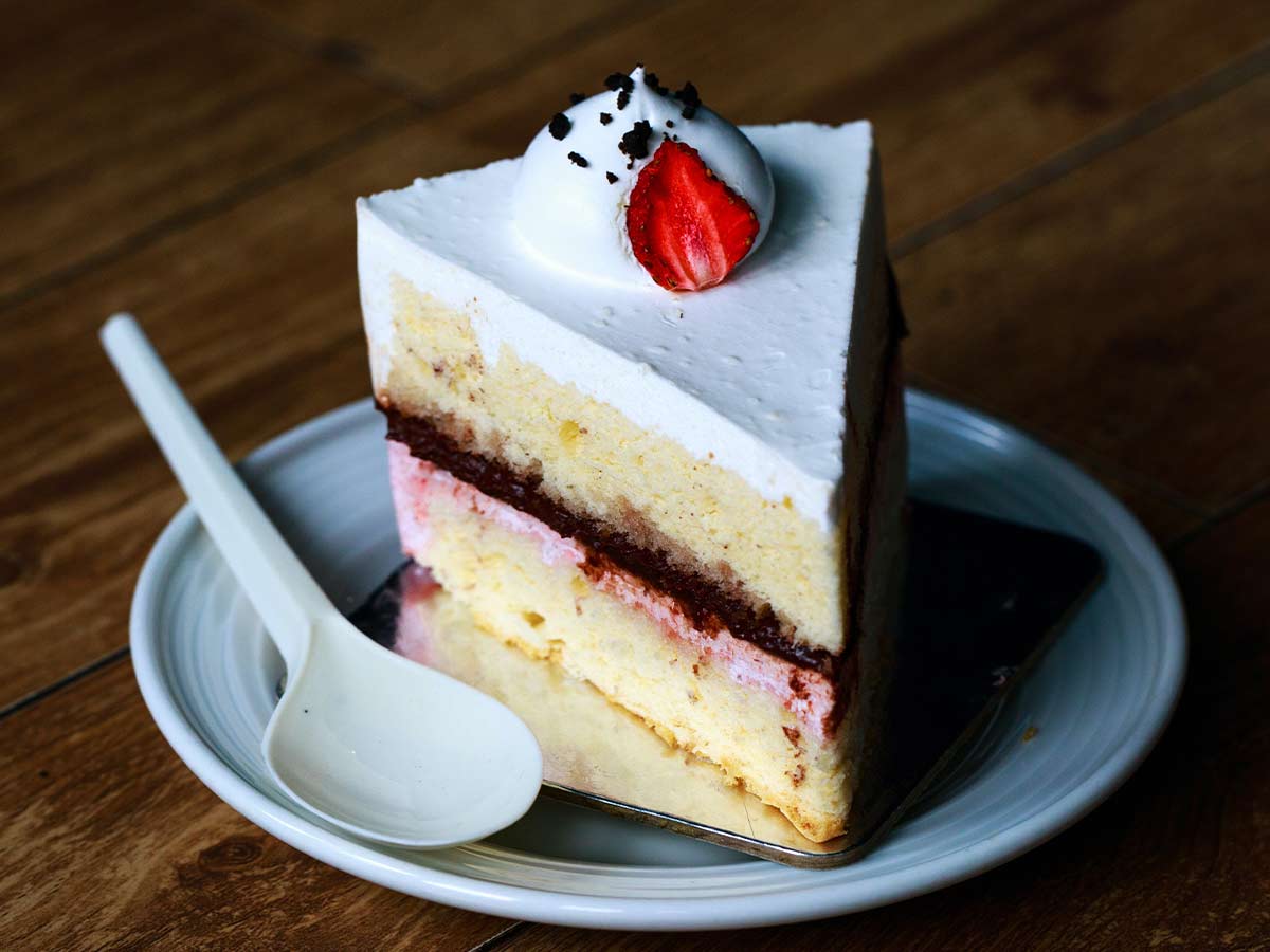 Slice of cake with white frosting, chocolate cookie crumb and a strawberry on top.