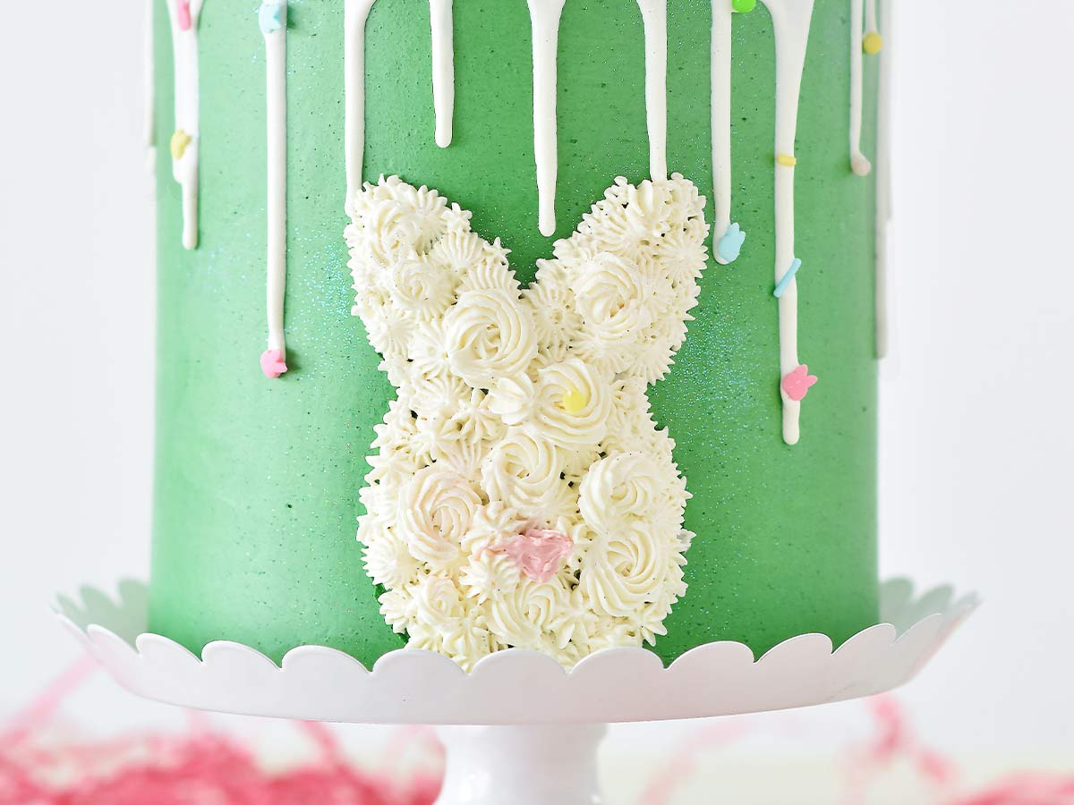 The side of a green birthday cake with white icing in the shape of a rabbit head.