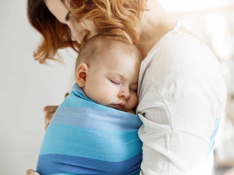 Mum cuddling her baby who is in a blue baby sling.