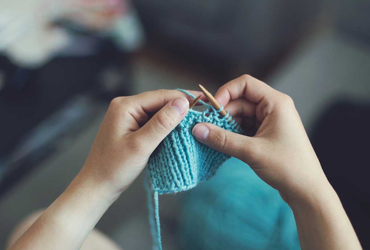 Young boy knitting with blue string.