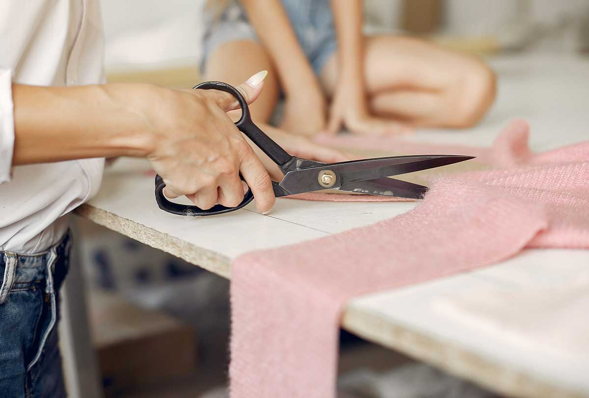 Close up of a mum cutting pink fabric to sew with her son.