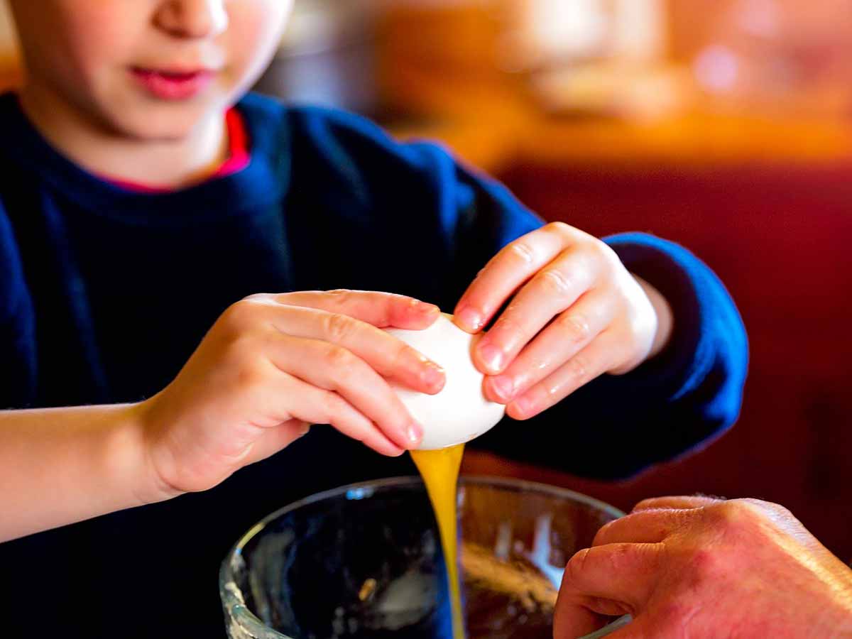 Close up of a boy cracking an egg into the bowl of cake mix to make a penguin cake.