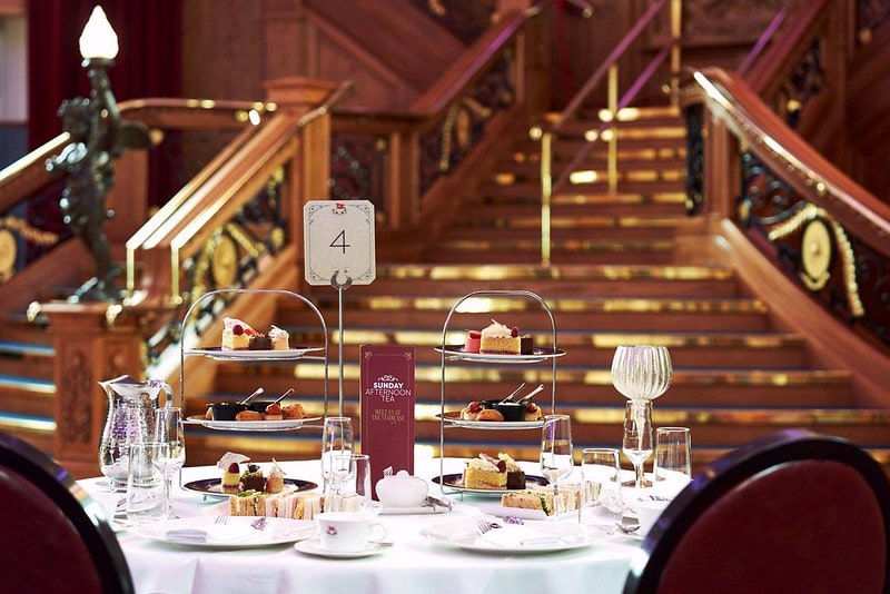 A table setting filled with sandwiches, savoury items, scones and cakes, positioned by the Grand Staircase at the Titanic Belfast.
