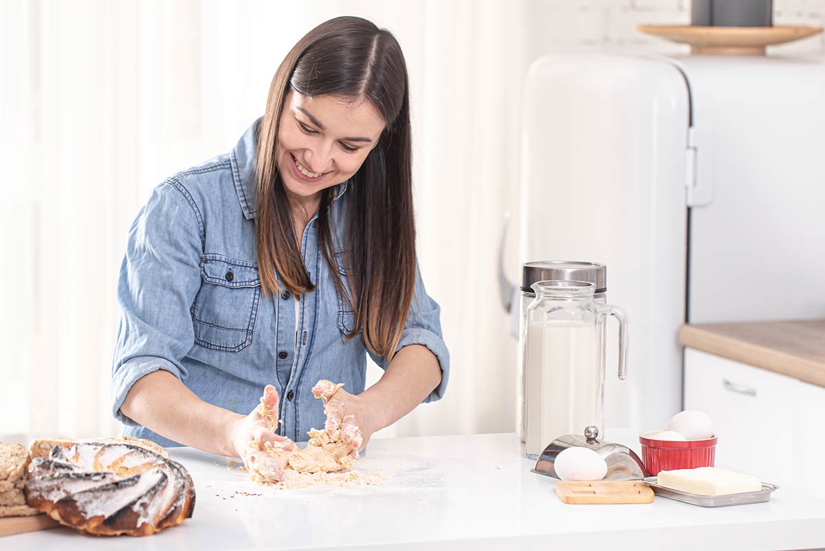 Woman smiling as she kneads dough with her hands on the kitchen counter.