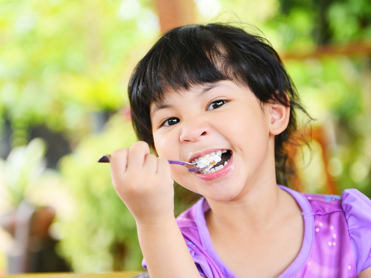 Girl wearing purple t shirt eating a piece of tardis cake in the garden.