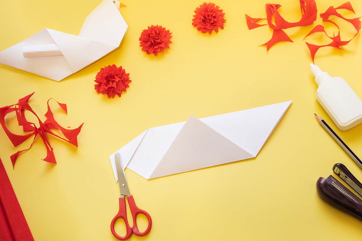 Supplies to make an origami swallow on a work top.