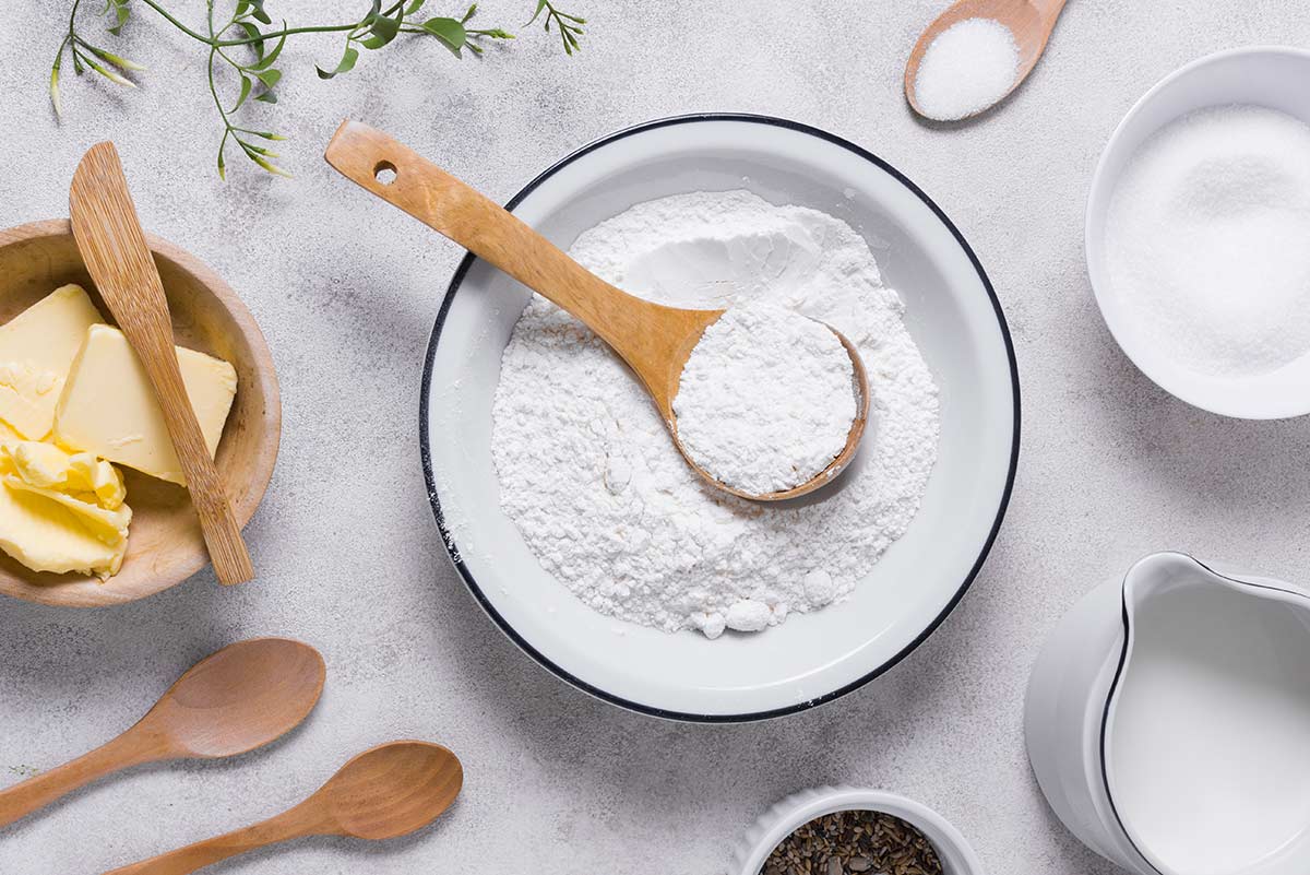 A bowl of flour on the table with other baking ingredients around it.