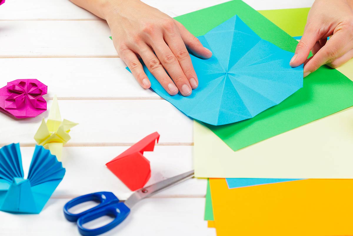 Close up of hands folding blue paper making origami.