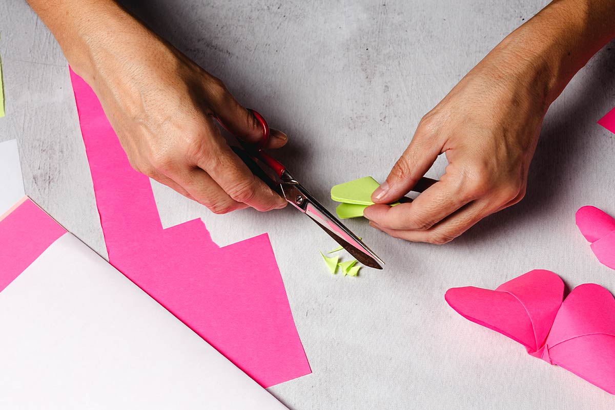Close up of hands cutting paper to make heart shapes.