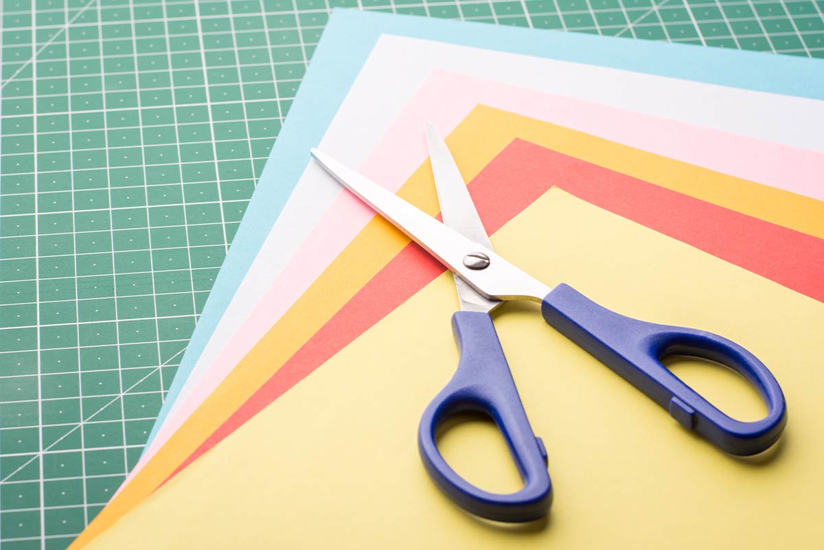 A pair of scissors on top of a pile of coloured paper fanned out.