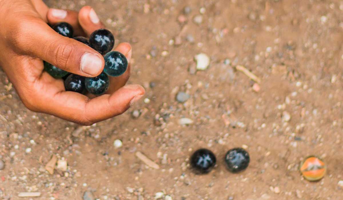 Hand holding marbles and rolling them along the ground.