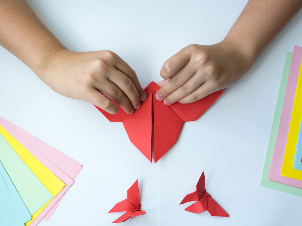 Close up of a child's hands folding red paper to make an origami hummingbird.