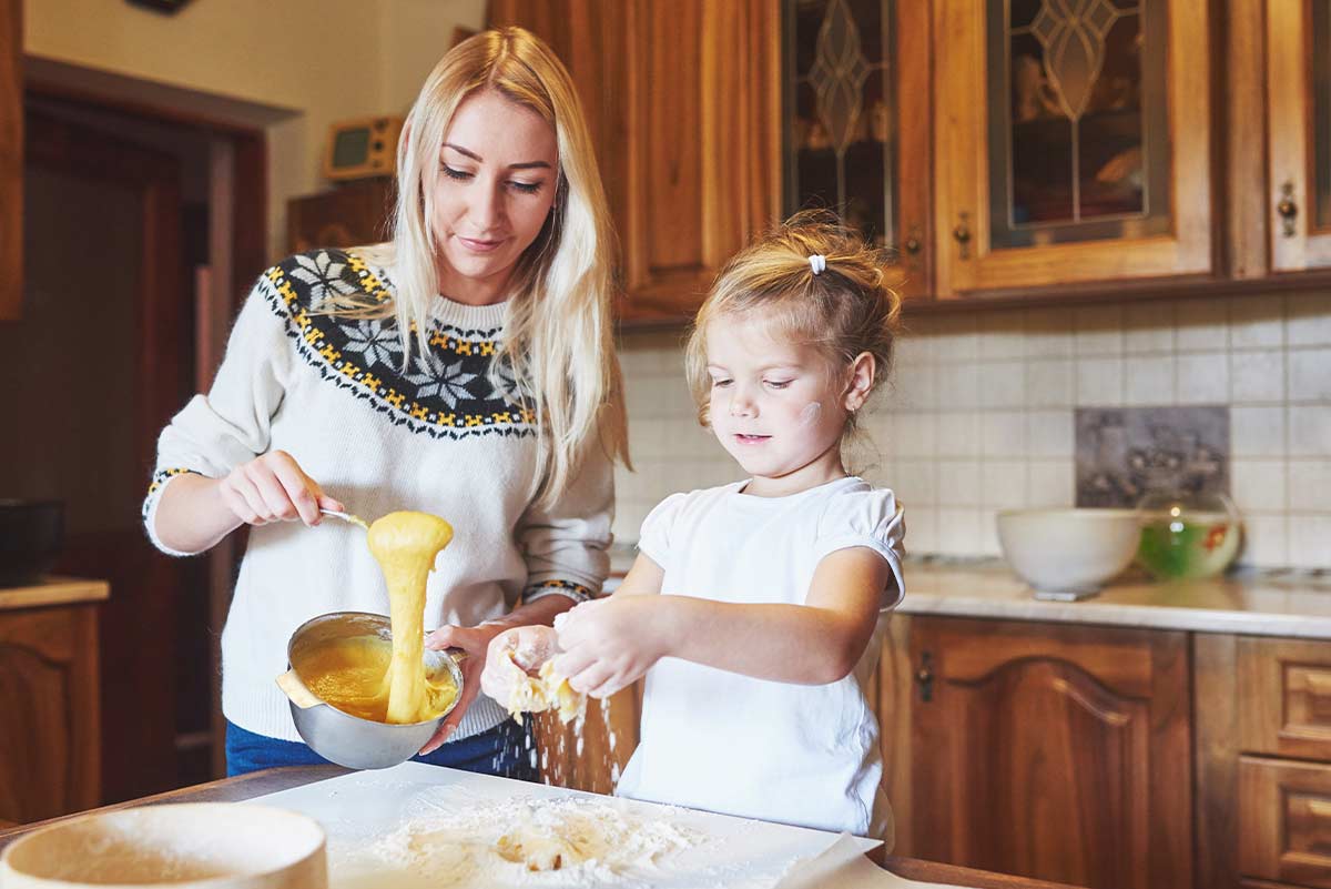 A mother and young daughter work together in their kitchen to bake a superman cake.