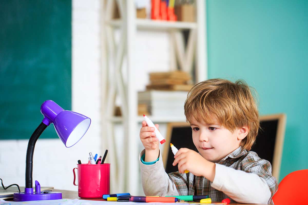 Young boy sat at the table with colouring felt tip pens.