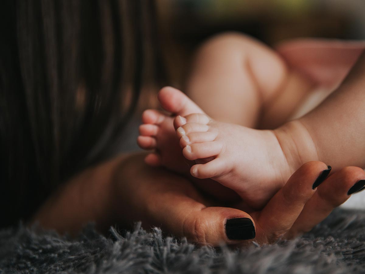 Mum, her nails painted black, with her palm open and her baby boy's feet resting in her hand.