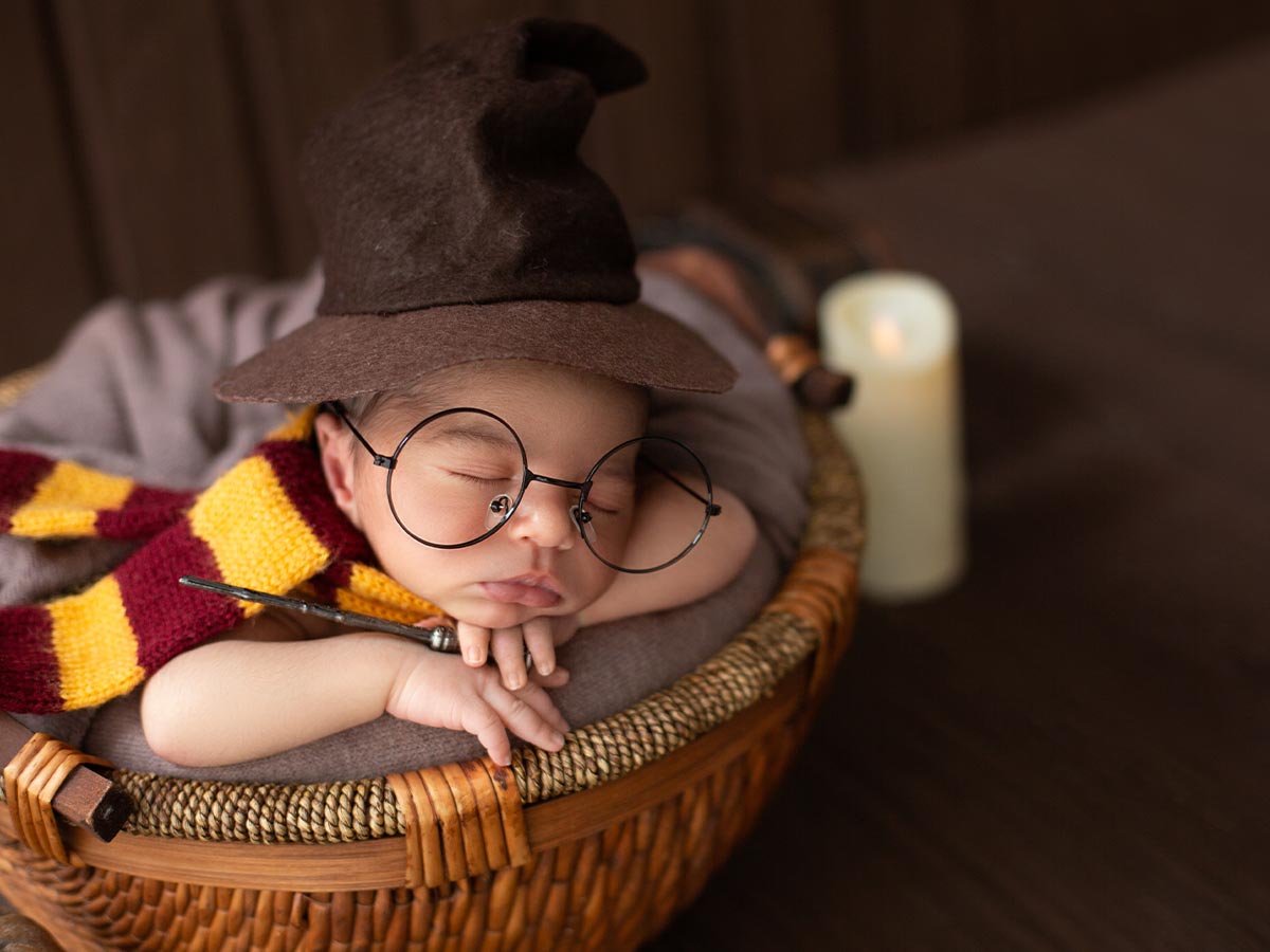 Baby boy wearing a Gryffindor scarf, sorting hat, Harry Potter glasses and holding a wand while he sleeps.