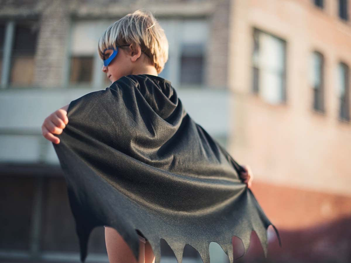 Young boy wearing a blue mask and a black cape.