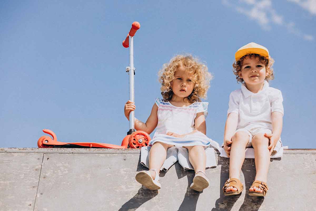 Two young children sat next to a scooter.