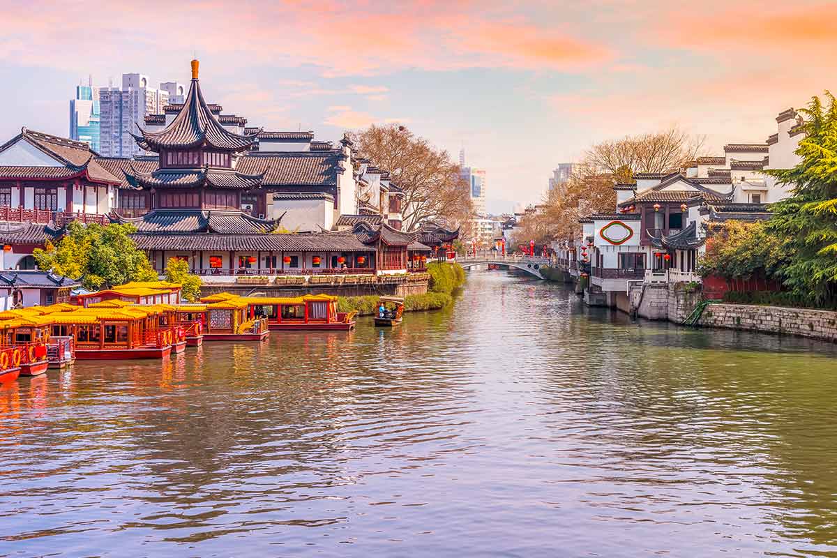 View of a Chinese riverside, traditional buildings on the river edge and high rise buildings in the distance.