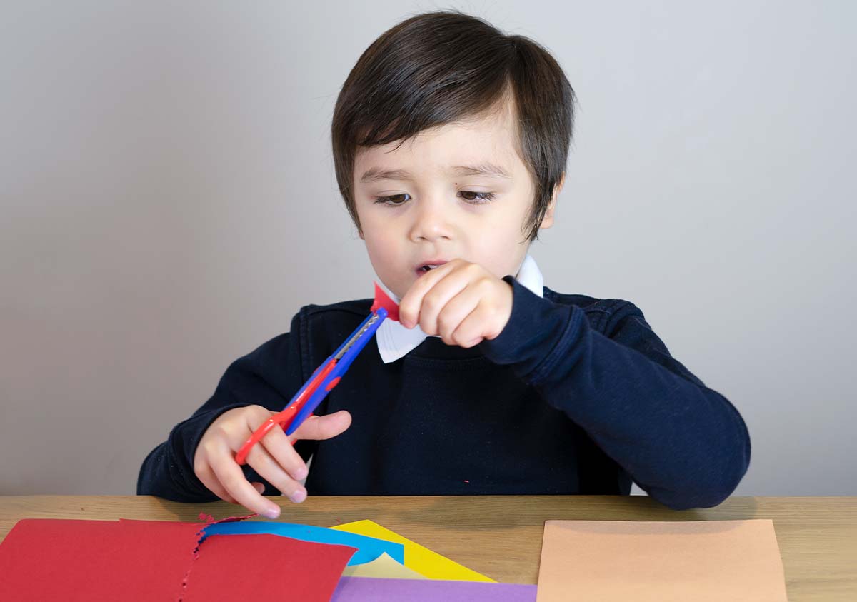 Little boy sat at a table cutting pieces of coloured paper to make a Gruffalo mask.