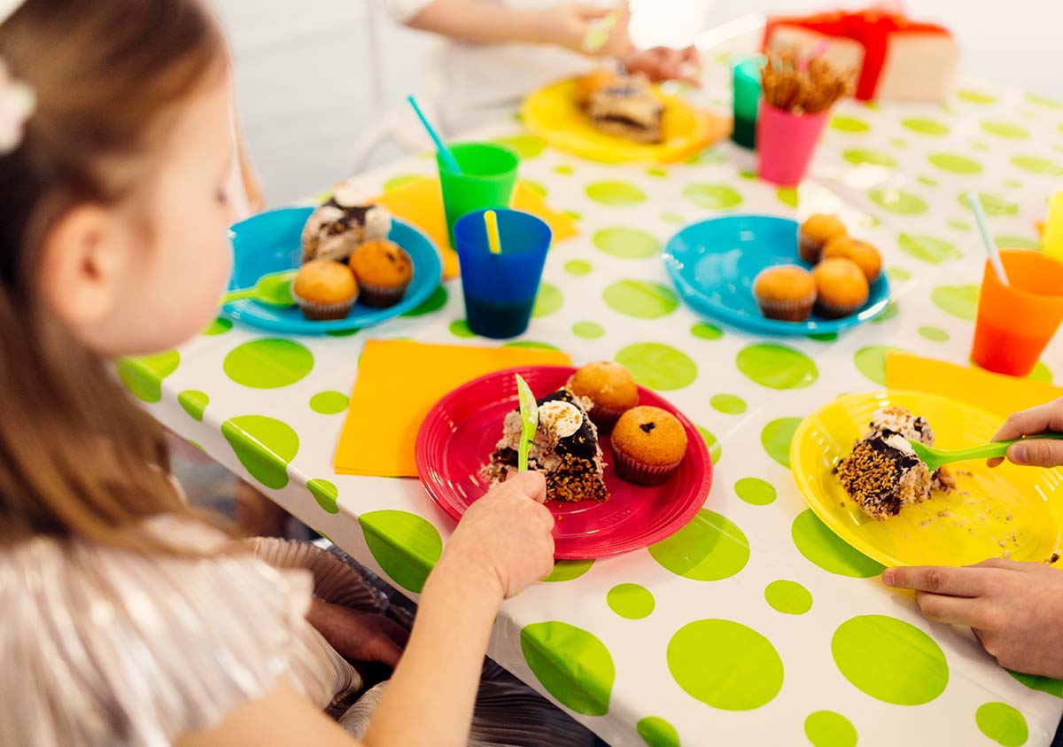 Little girl sat at the table eating a plate of birthday cake.