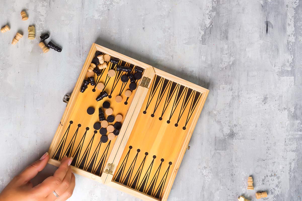 Hand resting on the corner of a small backgammon board.