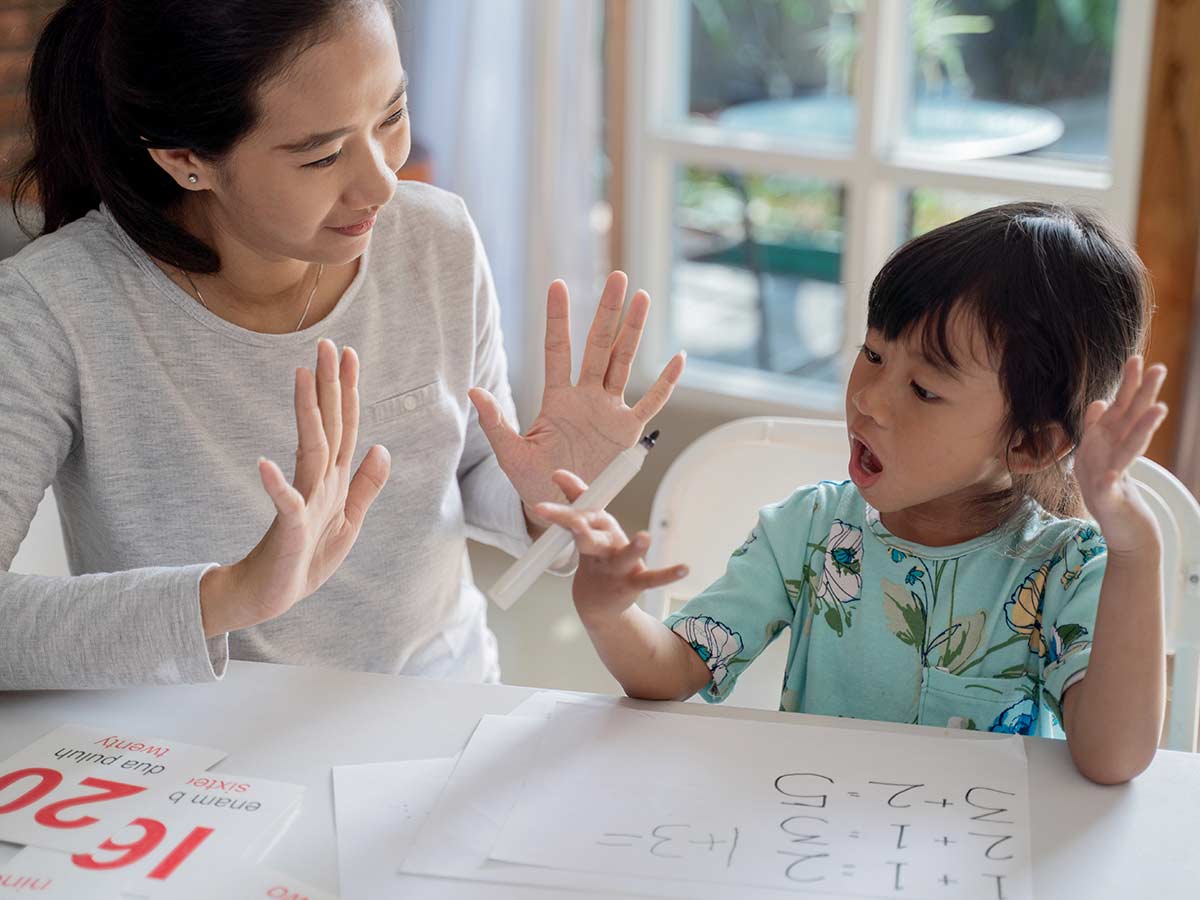 Mother and daughter are sitting at the table counting on their fingers to learn how to round numbers.