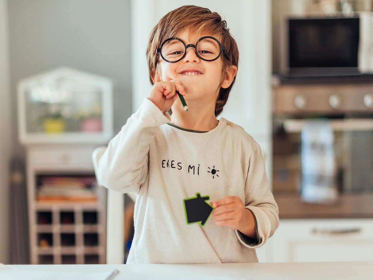A young boy wearing glasses and holding a pencil smiles proudly at the camera after learning how to round numbers.