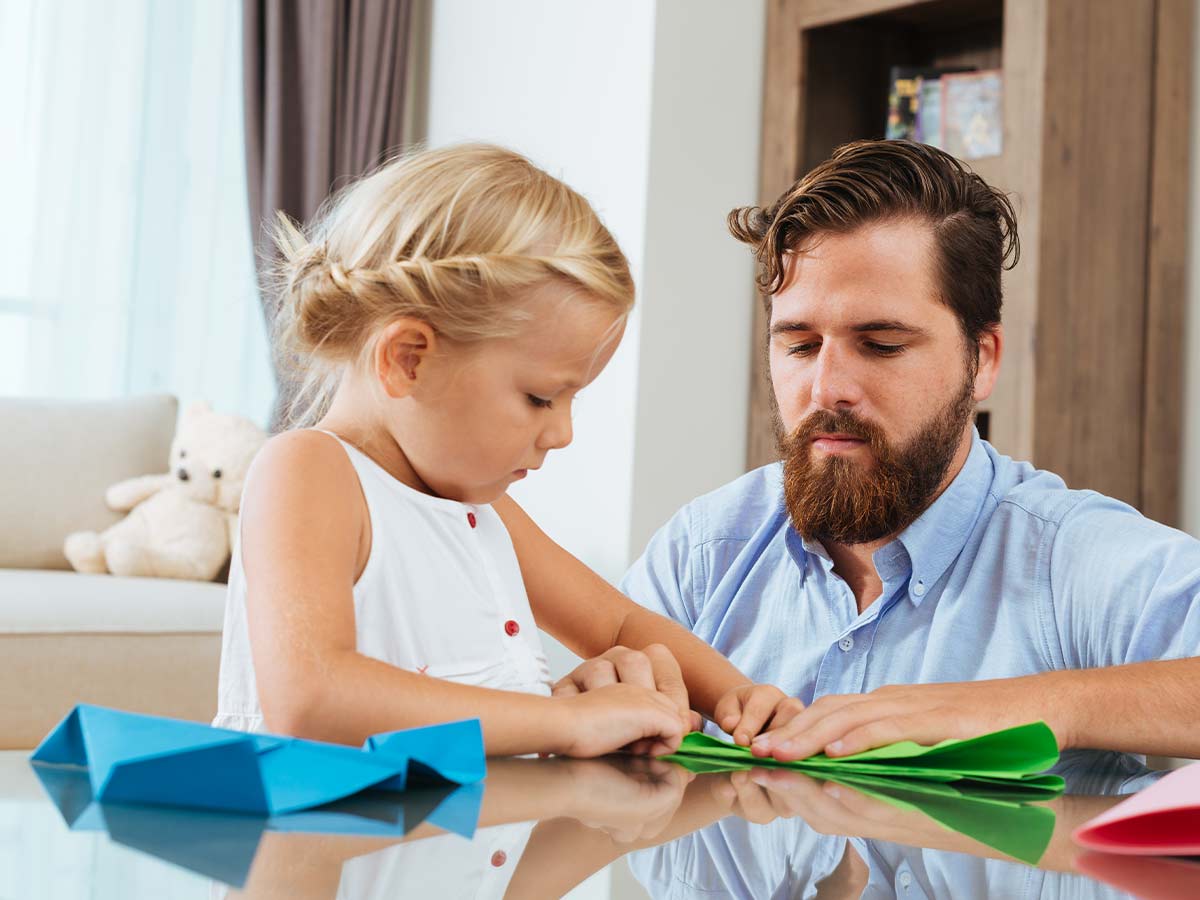 Little girl sat at the table making DIY flower wreaths with her dad.