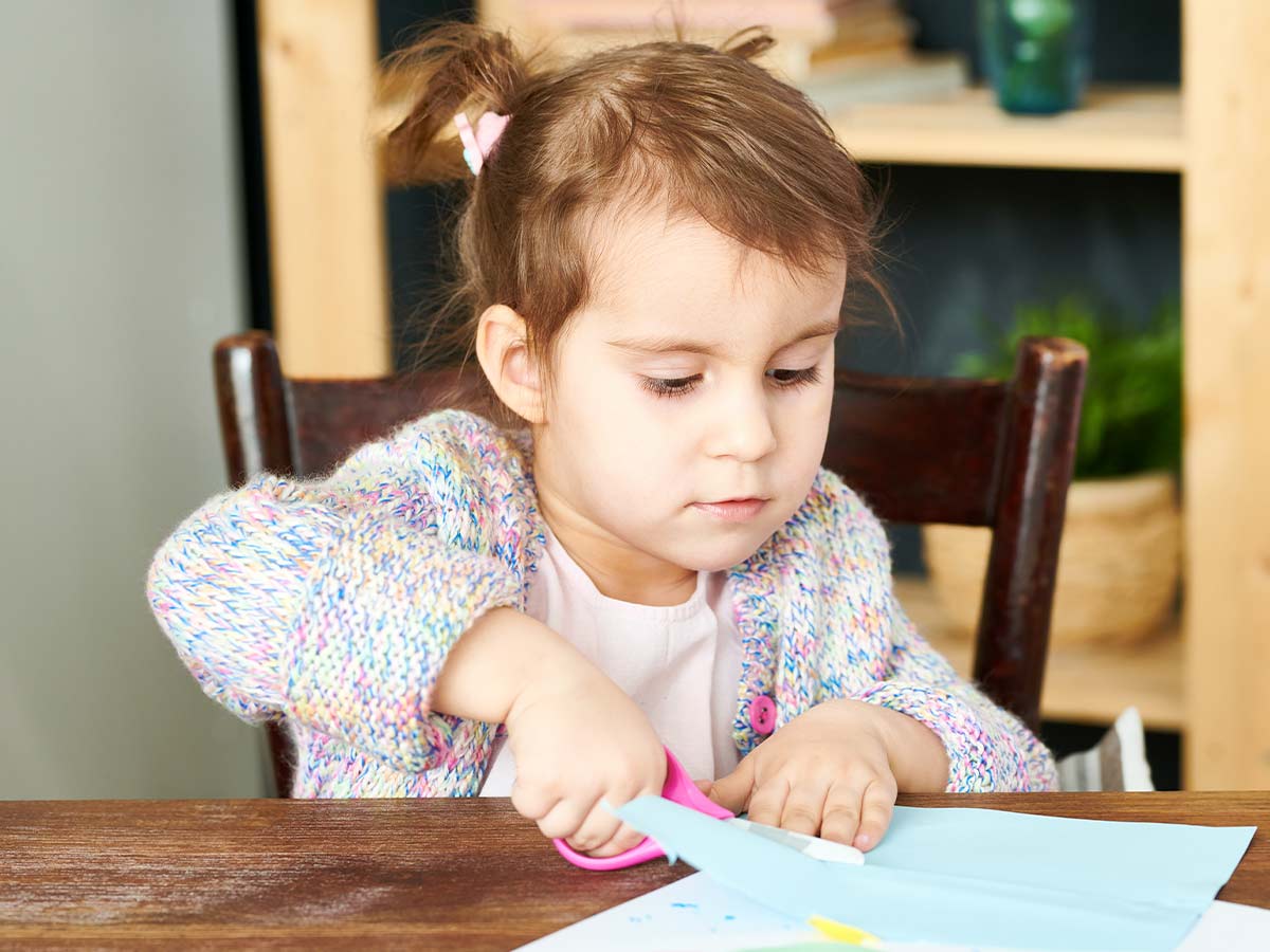 Little girl sat at the table cutting paper to make a DIY flower wreath.