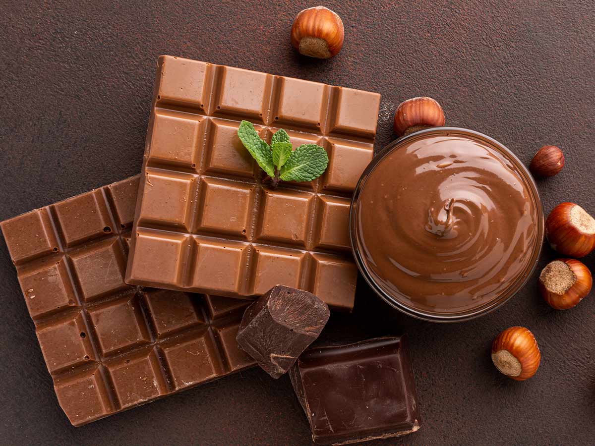 A selection of different types of chocolate, melted and solid, on the table with some hazelnuts.