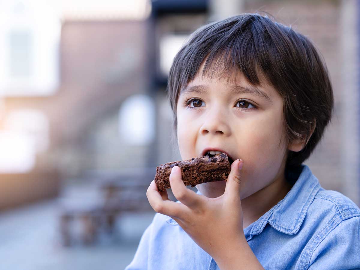 A little boy with dark hair and wearing a blue shirt taking a bite of a piece of chocolate pinata cake.e