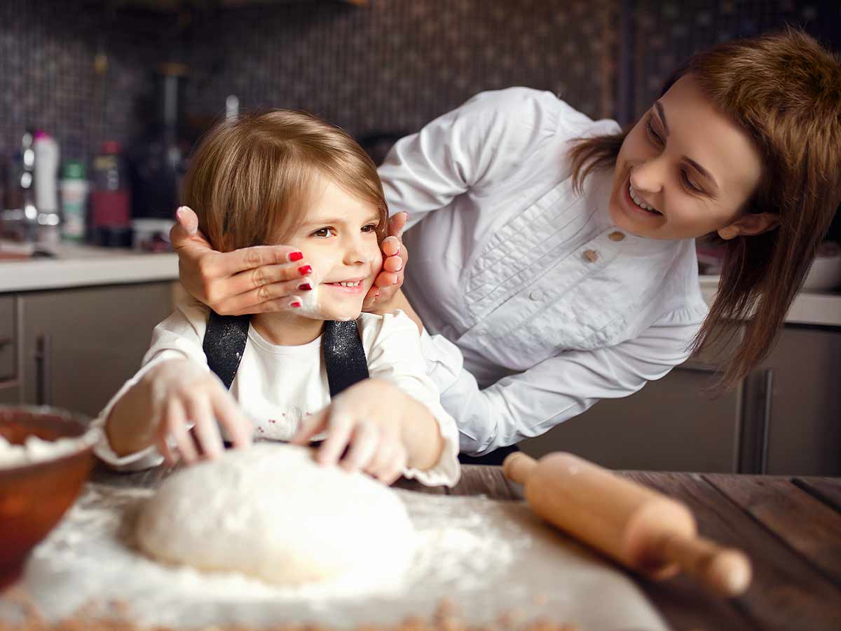 Mum rubbing flour on her son's face while they're in the kitchen baking a Postman Pat cake.