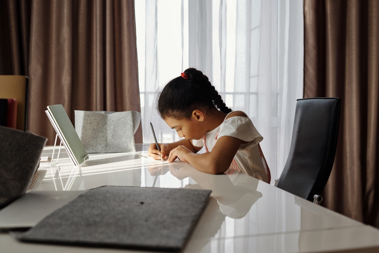A young girl is sitting at her desk, writing and practising using idioms.