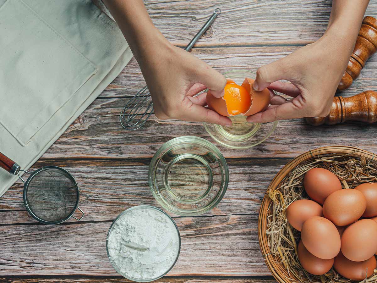A close up of someone breaking eggs into a bowl to make a LEGO cake, surrounded by other ingredients.