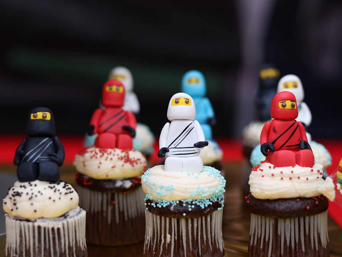 Lots of chocolate cupcakes with white icing with LEGO figure fondant cake toppers placed on top.