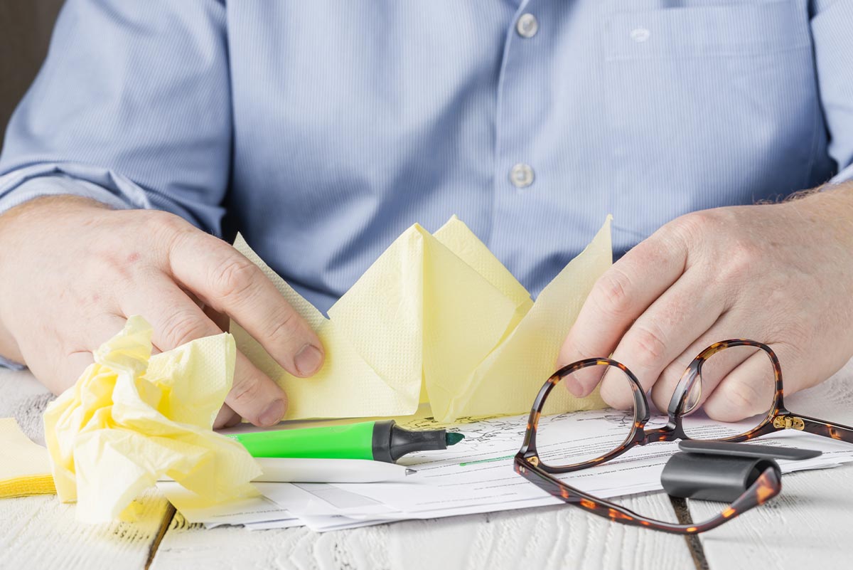 Man at table trying to fold an origami rhino that stands up.