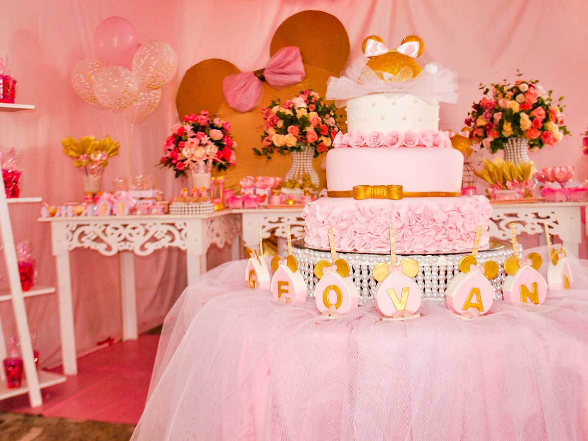A pink layered princess cake o a display table at a princess party, surrounded by pink flowers, balloons and other decorations.e