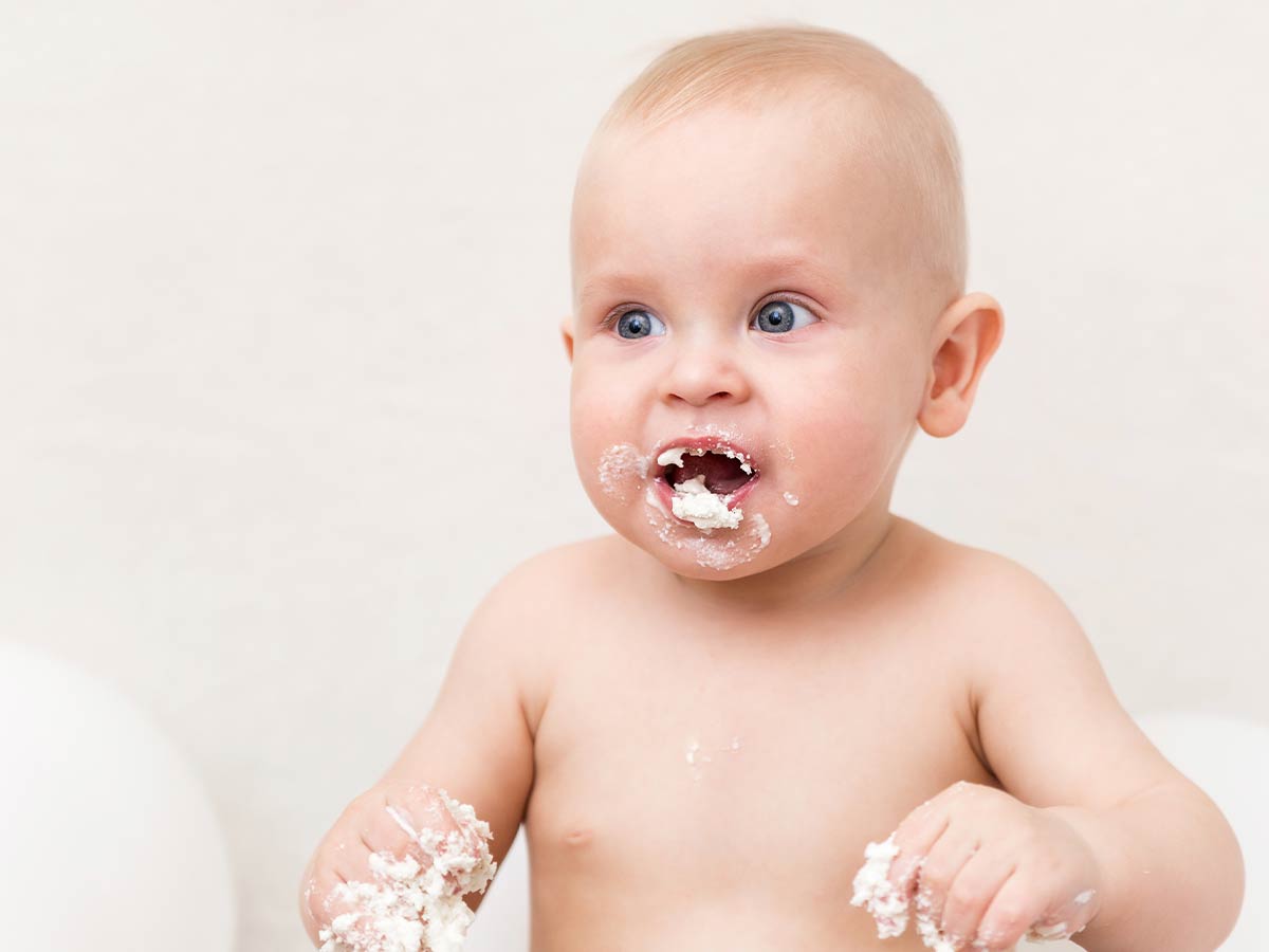 Cute baby with a messy mouth and hands after enjoying a taste of ladybird cake.