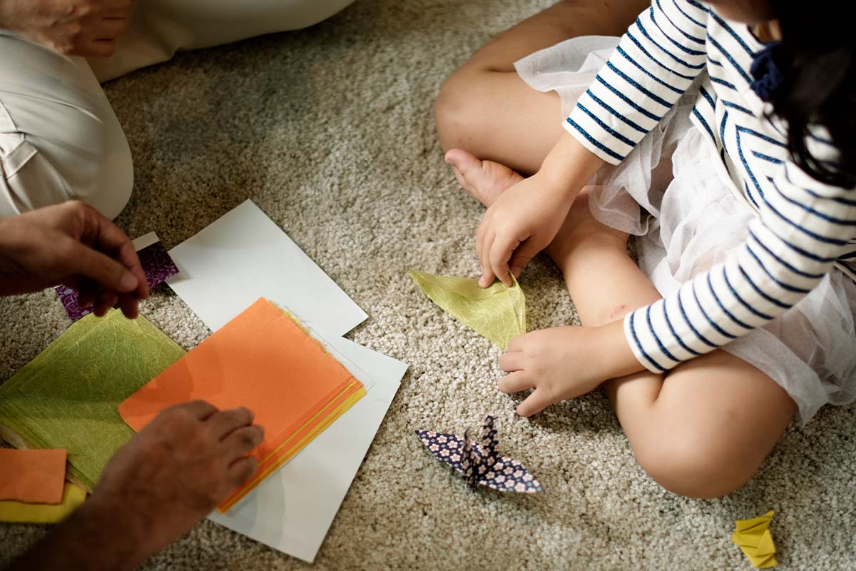 Overhead shot of a child and adult sitting on the floor folding paper to make an origami penguin.