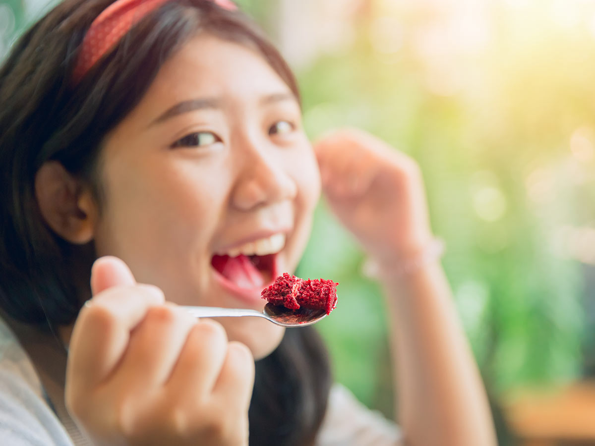 Teenage girl eating a bite of red velvet laptop cake.