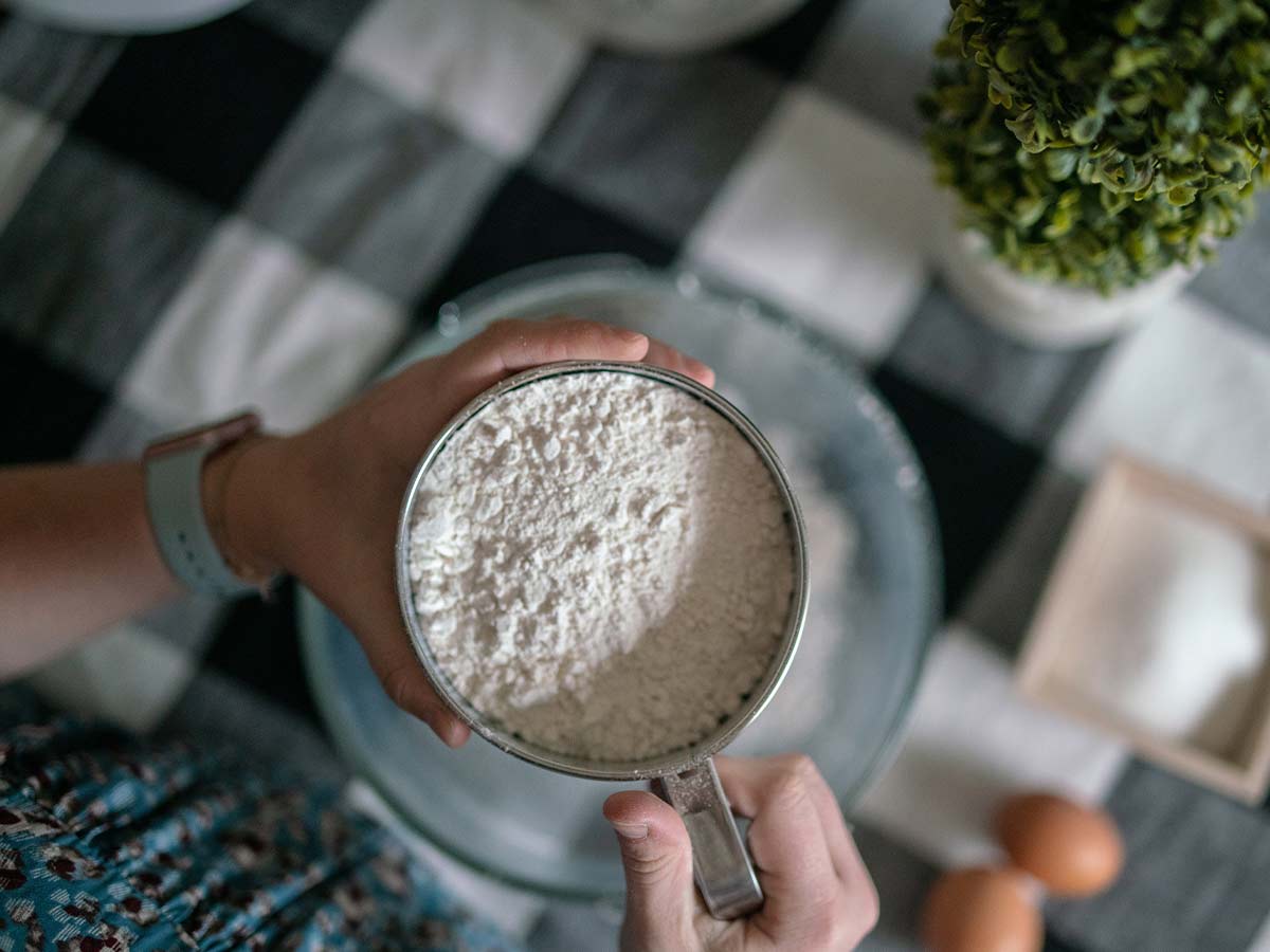 Person holding a bowl of flour over the mixing bowl for the Scooby Doo cake batter.