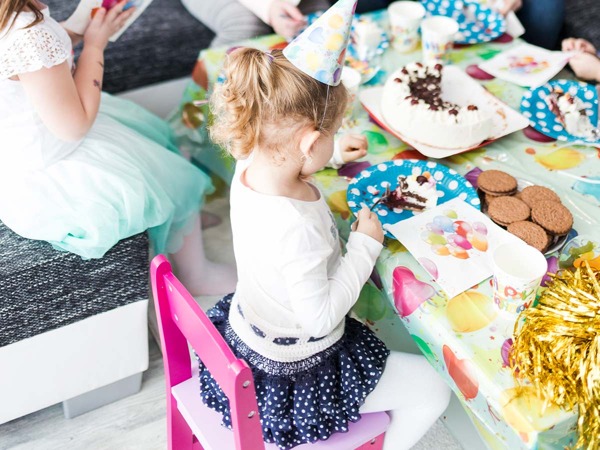 Little girl at a birthday party wearing a party hat sat at the table eating some Scooby Doo cake.