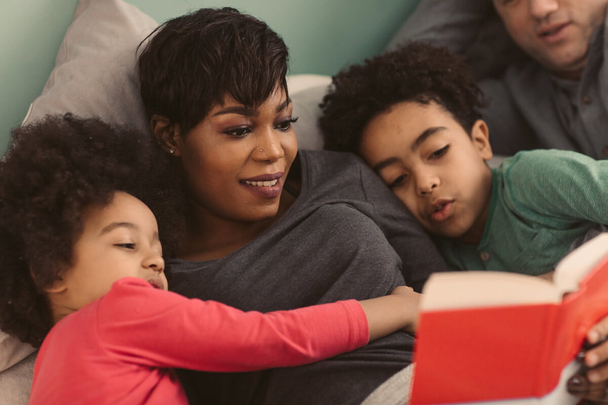Family lying on the sofa, the mum reading with the two kids so that they can write a book review.
